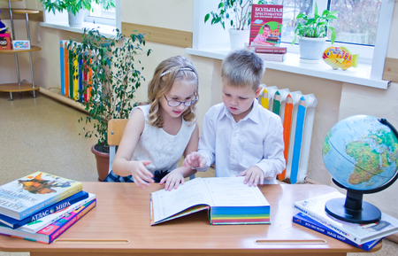 Two small schoolchildren, boy and girl sitting together at the desk in classroom, reading the study book - Russia, Moscow, first high school, 2 class b - October 28, 2017のeditorial素材