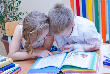 Two small schoolchildren, boy and girl sitting together at the desk in classroom, reading the study book - Russia, Moscow, first high school, 2 class b - October 28, 2017のeditorial素材
