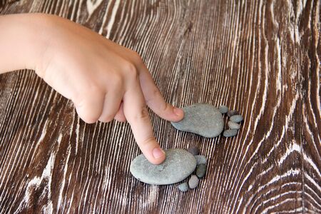 stones lie in the shape of a foot with five fingers on a wooden table macro photographyの写真素材