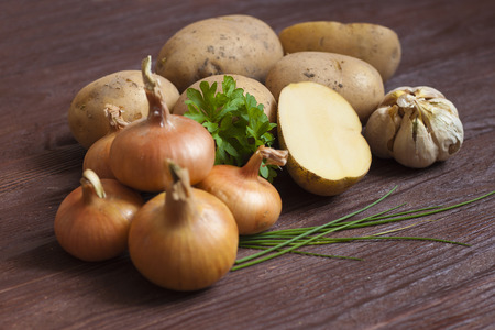 Potatoes, onions, garlic and parsley on a wooden boardの写真素材