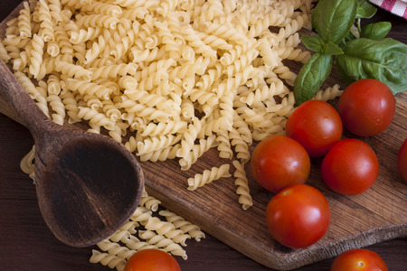 Dried pasta, tomatoes and basil on wooden backgroundの写真素材