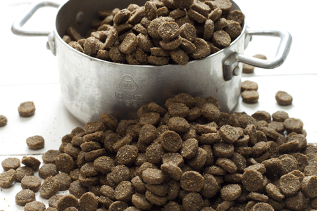 A small metal bowl of dog food spilling onto a white deskの写真素材