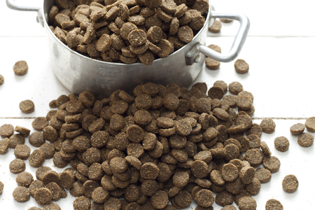 A small metal bowl of dog food spilling onto a white deskの写真素材