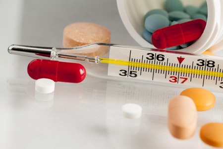 Thermometer with pills and capsules isolated on white background