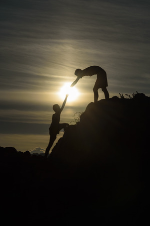 Silhouette of two boys helped pull together climbingの写真素材