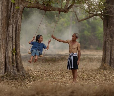 Happy family.Laughing  father and daughter are playing swing under treeの写真素材