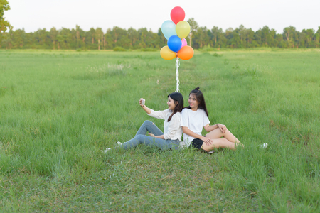 girl with balloons in the green field. Two smiling girls selfie with balloonsの写真素材