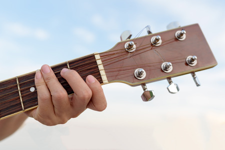 Close-up of woman's hands playing guitar on blue sky backgroundの写真素材