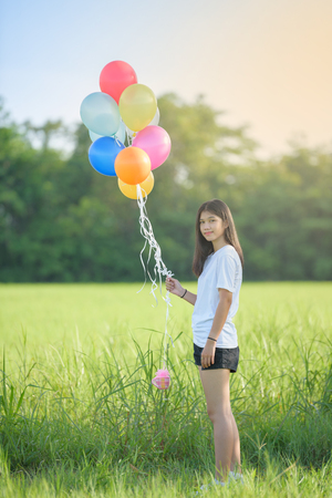 girl with balloons in the green field. Smiling girl play with balloons happilyの写真素材