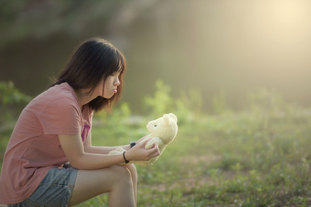 Portrait of a beautiful young girl is playing with teddy bear outdoor during sunsetの写真素材