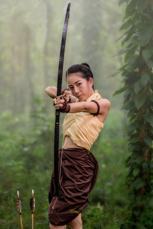 Beautiful ancient archery woman with bow and arrows aiming in forest background