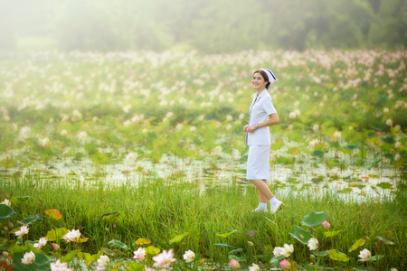smiling beautiful nurse is walking on lotus flower field during sunriseの写真素材