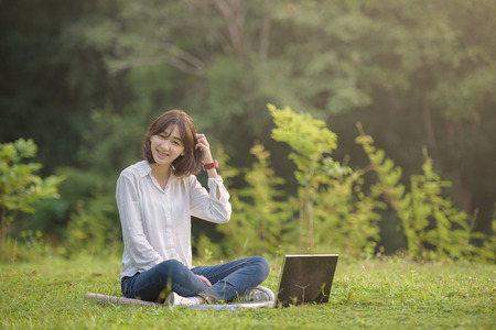 beautiful female student with laptop working outdoor with beautiful light and nature backgroundの写真素材