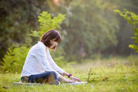 beautiful caucasian college student with laptop working outdoor with beautiful light and nature background, beautiful caucasian texting on laptopの写真素材