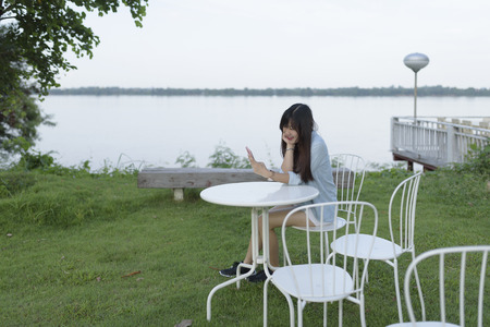 Portrait of young woman use mobile phone while sitting outdoor, smiling happy female reading on cell telephone, woman typing text message on smart phone in outdoor cafe, image of young woman sitting at a table using mobile phone.の写真素材
