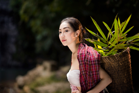 portrait of beautiful Asian woman in traditional costume carrying basket of herb waiting for someoneの写真素材