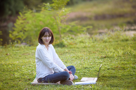 beautiful caucasian college student with laptop working outdoor with beautiful light and nature background, beautiful caucasian texting on laptopの写真素材