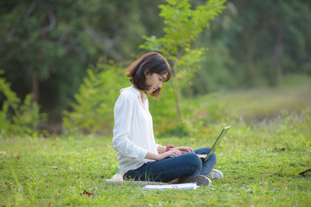 beautiful caucasian college student with laptop working outdoor with beautiful light and nature background, beautiful caucasian texting on laptopの写真素材