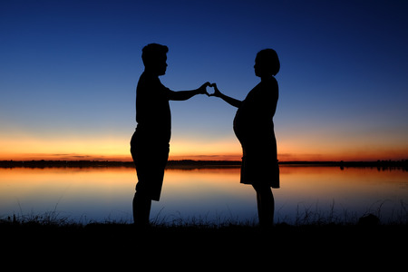 silhouette of dad and pregnancy mom at sunset with beautiful nature backgroundの写真素材