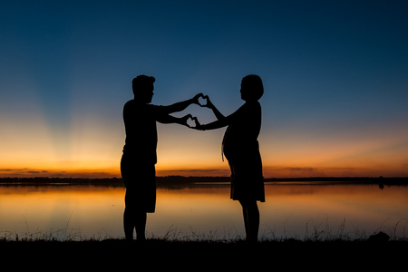 silhouette of dad and pregnancy mom at sunset with beautiful nature backgroundの写真素材