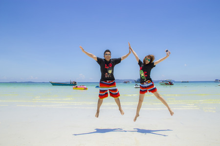 smiling couples are jumping high in beach with blue sky and sea backgroundの写真素材
