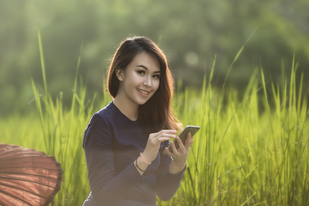 eyes contact of smiling beautiful farmer is using smartphone in ricefieldの写真素材