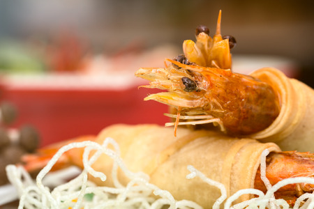 Close up of Fried Shrimps wrapped and crispy fried noodles with various food as background with warm light flareの写真素材