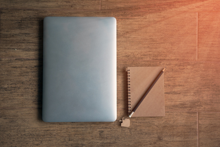 Laptop and notebook placing together on wooden table by flat lay; warm ray light flare from windowの写真素材