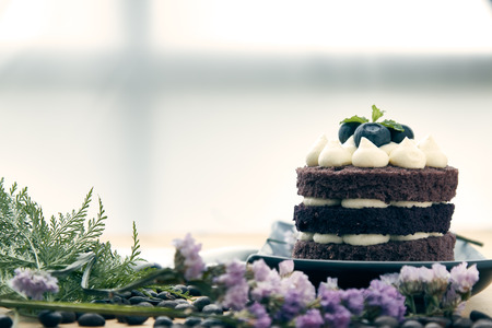 Brown cake with berry on top placing with pink flower as decorated item on the wooden tableの写真素材