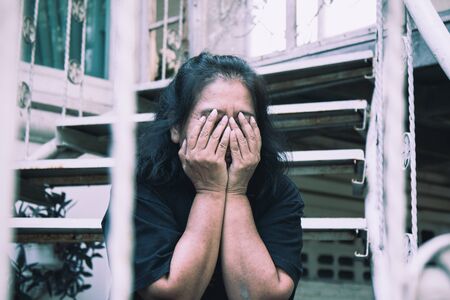 The old woman place her hands on face and express worried feeling while sitting on stairs