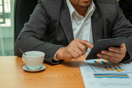 40s Asia businessman holding taplet and searching the information while checking the sales report in...