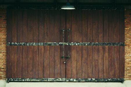 Old warehouse as dark brwon wooden sliding door with brown brick wall and lampの写真素材