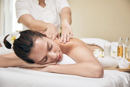 Young Asian beautiful woman lying down on bed and getting oil massaging treatmentの写真素材