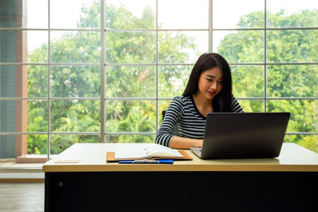 Happy young Asian woman smiling and using laptop in living room by working from home concept with copy spaceの写真素材