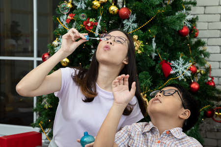 Asian young sister blow bubble from stick with child in living room with Christmas decoration tree