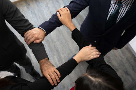 close up of joining hands of businessman in unity cross processing background in office; Expression for cooperationの写真素材
