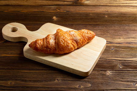Tasty French croissant. Freshly baked croissants with cutting wooden plate on brown rustic wood board backgroundの写真素材