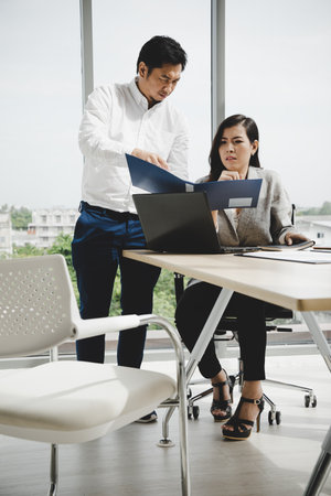 Asian manager holding and pointing file to ask question sale woman summary report in meeting roomの写真素材