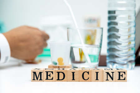 Close up medicine wooden block word on table with tablet and drinking water for female patientの写真素材