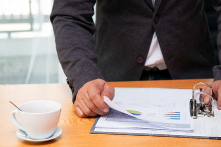 Asian young businessman holding finding sales data sheet paper from file on desk in officeの写真素材