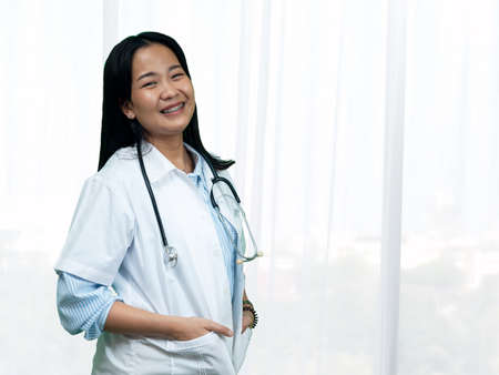 Young female Asian happiness doctor in uniform with stethoscope standing in hospital roomの写真素材