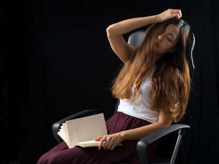 Young Asian brown hair female in white shirt sitting chair tired sleeping lonely touching head with copy space on black backgroundの写真素材