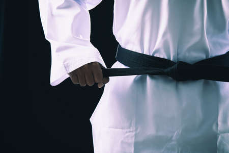 Close up Taekwondo martial arts fighter in white uniform holding black belt on dark backgroundの写真素材