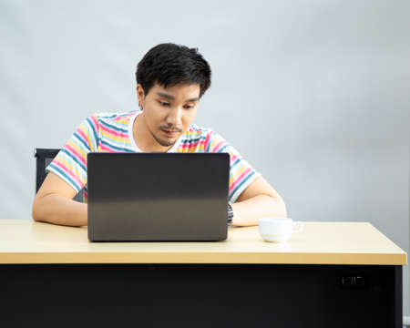 Handsome young beauty male model portrait wear rainbow T shirt sitting and using laptop in living roomの写真素材