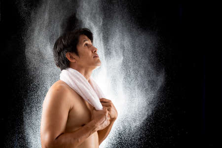 Young Asian handsome sporty man with white towel holding on splash water drop black background with...
