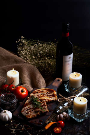 pork chops steak with black pepper sauce placing on vintage wooden plate together with many ingredient and wine bottle in dark backgroundの写真素材