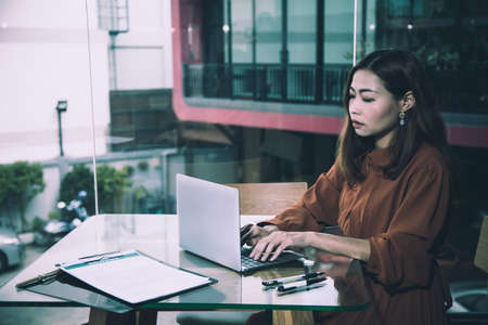 Young Asian adult brown hair woman sitting in cafe and typing using laptop concentrate stress emotionの写真素材