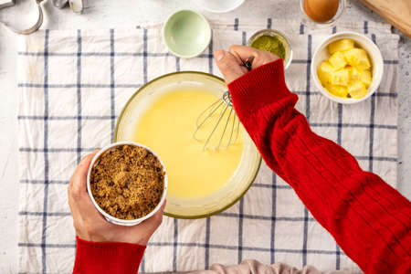 Woman hand in red long sleeve using egg beater stir mixing ingredient in glass bowl and holding...