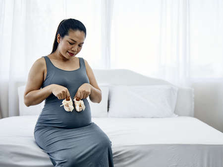 Small shoes for the unborn baby with bow tie; Pregnant woman holding small baby shoes relaxing...