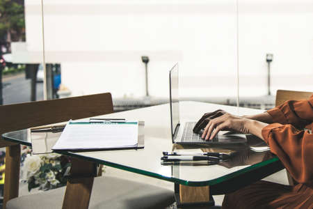 Yonug adult brown hair woman sitting in cafe and typing using laptop checking insurance agreementの写真素材